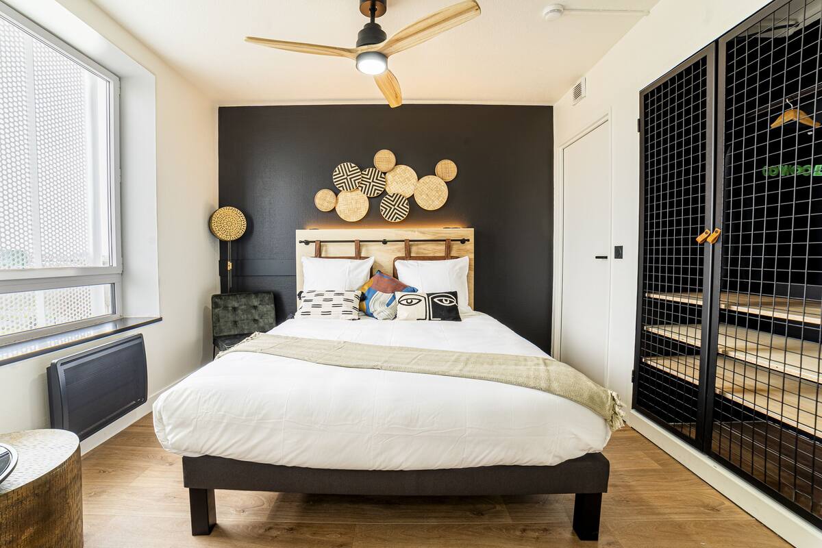 Une chambre à coucher avec un lit, un ventilateur de plafond, une fenêtre et un portail en métal noir.