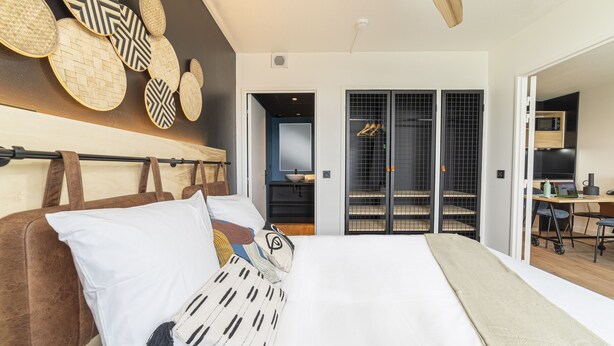 A modern bedroom with a large bed, a ceiling fan, and a view into a kitchen area. - Cowool Toulouse (Toulouse)