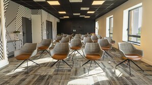 A conference room with rows of grey upholstered chairs with brown seats, a patterned carpet, and large windows along one wall. - Cowool Toulouse (Toulouse)
