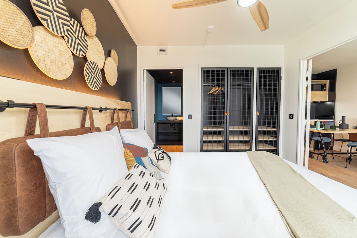 Une chambre moderne avec un grand lit, un ventilateur de plafond et une vue sur un coin cuisine.