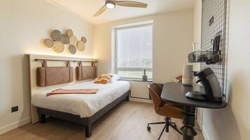A modern bedroom with a bed, a desk, a chair, a ceiling fan, and a window with blinds.