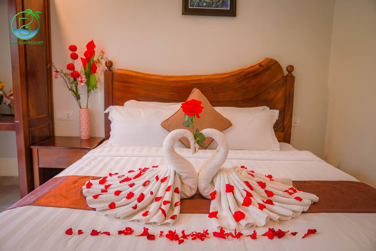 A neatly made bed with a wooden headboard, a decorative pillow, and a bouquet of red roses.