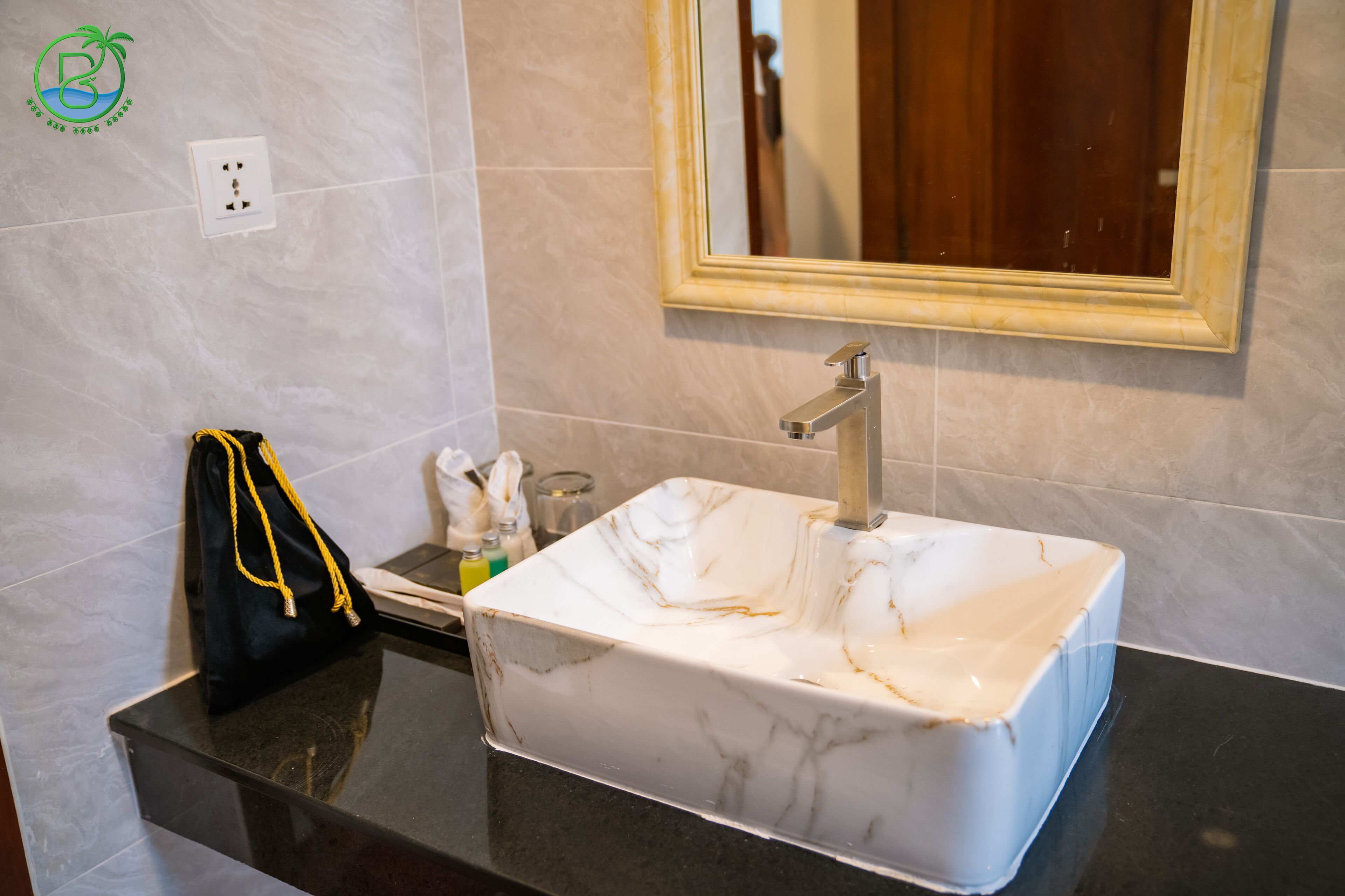 Un baño con lavamanos de mármol blanco, un espejo y encimera negra.