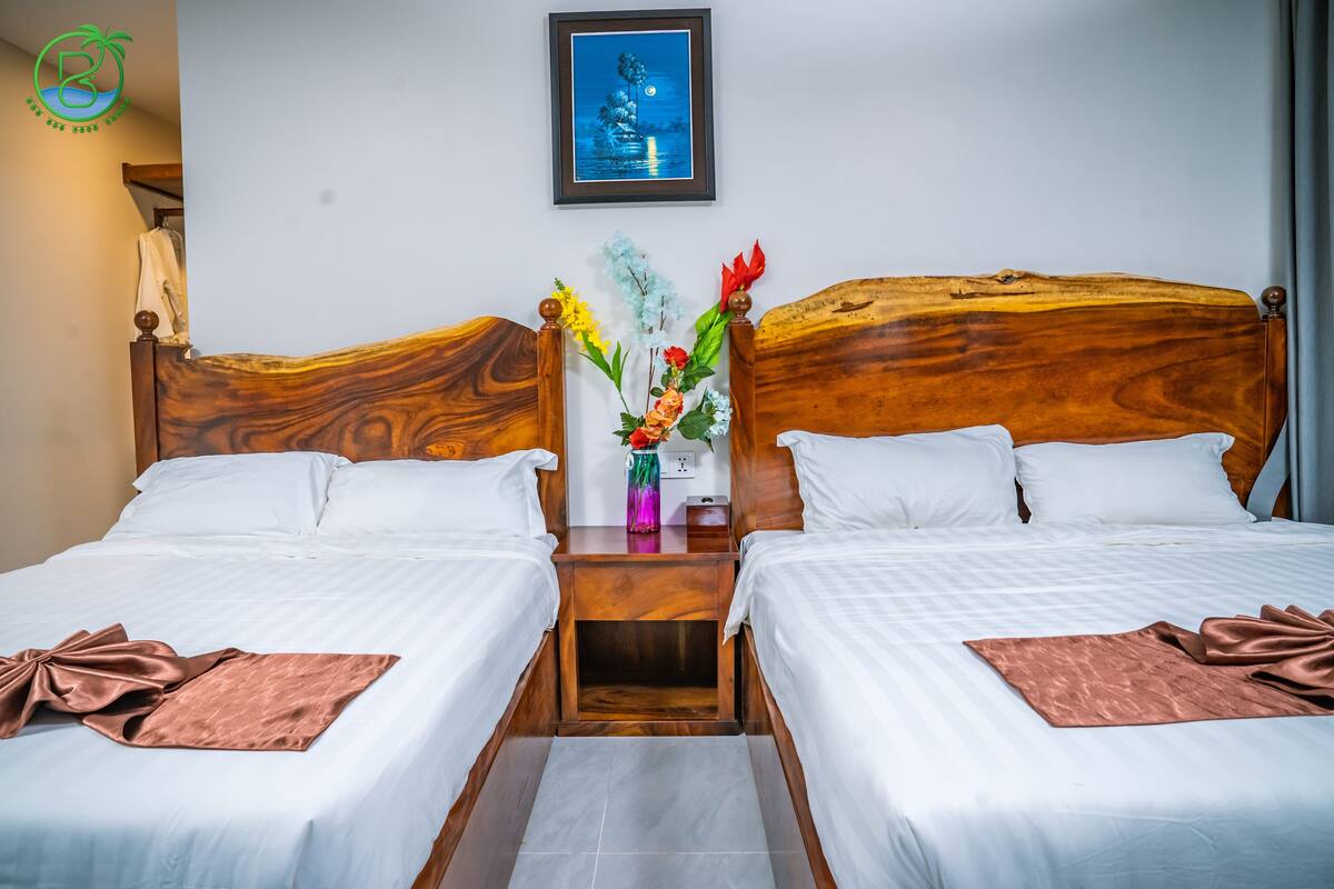 A hotel room with two single beds, a nightstand with a vase of flowers, and a framed picture on the wall.