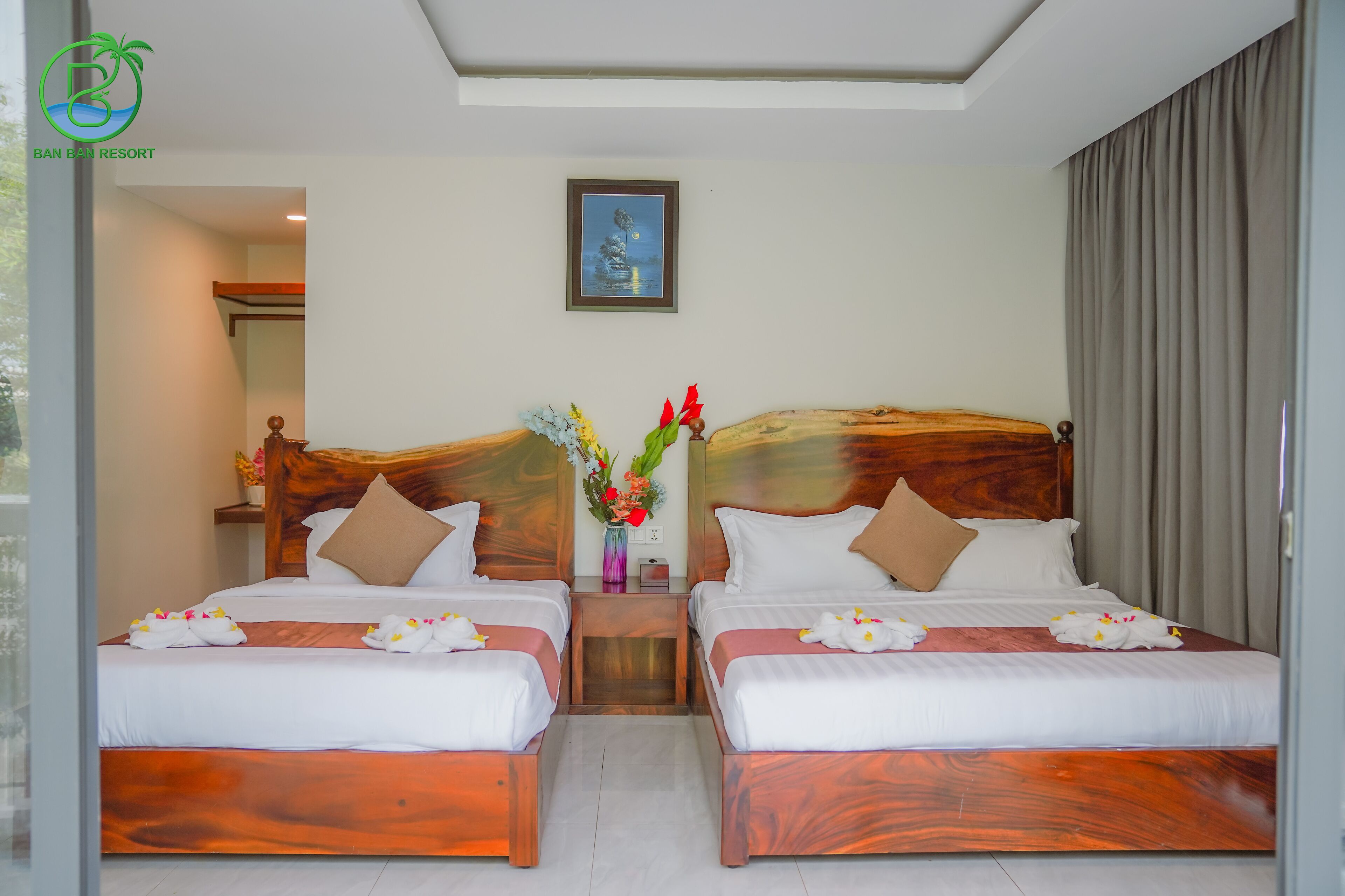 Ein Hotelzimmer mit zwei Betten, Holz-Kopfteilen, weißer Bettwäsche, einer Vase mit Blumen und einem Bild an der Wand.