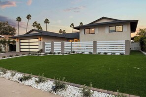 A modern two-story house with a garage, a well-maintained lawn, and a white fence.