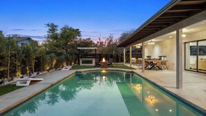 Un espace piscine extérieur moderne doté d’un foyer, d’un coin repas couvert et offrant une vue sur le paysage environnant.