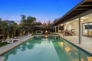 A modern outdoor pool area with a fire pit, a covered dining area, and a view of the surrounding landscape.