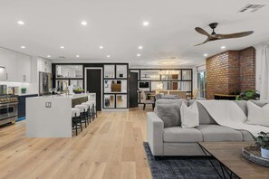 A modern kitchen with a central island, a dining area with a brick wall, and a living room with a sofa and a ceiling fan. - Valley View: Chic Design w/ Pool, Grille, Firepit (Scottsdale)