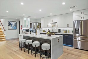 A modern kitchen with a central island, bar stools, stainless steel appliances, and white cabinetry. - Valley View: Chic Design w/ Pool, Grille, Firepit (Scottsdale)
