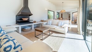 Uma sala de estar moderna com lareira embutida, um sofá branco, uma mesa de centro e uma porta de vidro que dá para uma área externa.