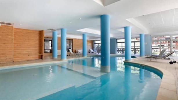 An indoor swimming pool with blue pillars, lounge chairs, and a wooden wall. - T2 Montagne Cosi Pied des Pistes- Piscine Hammam (Allos)