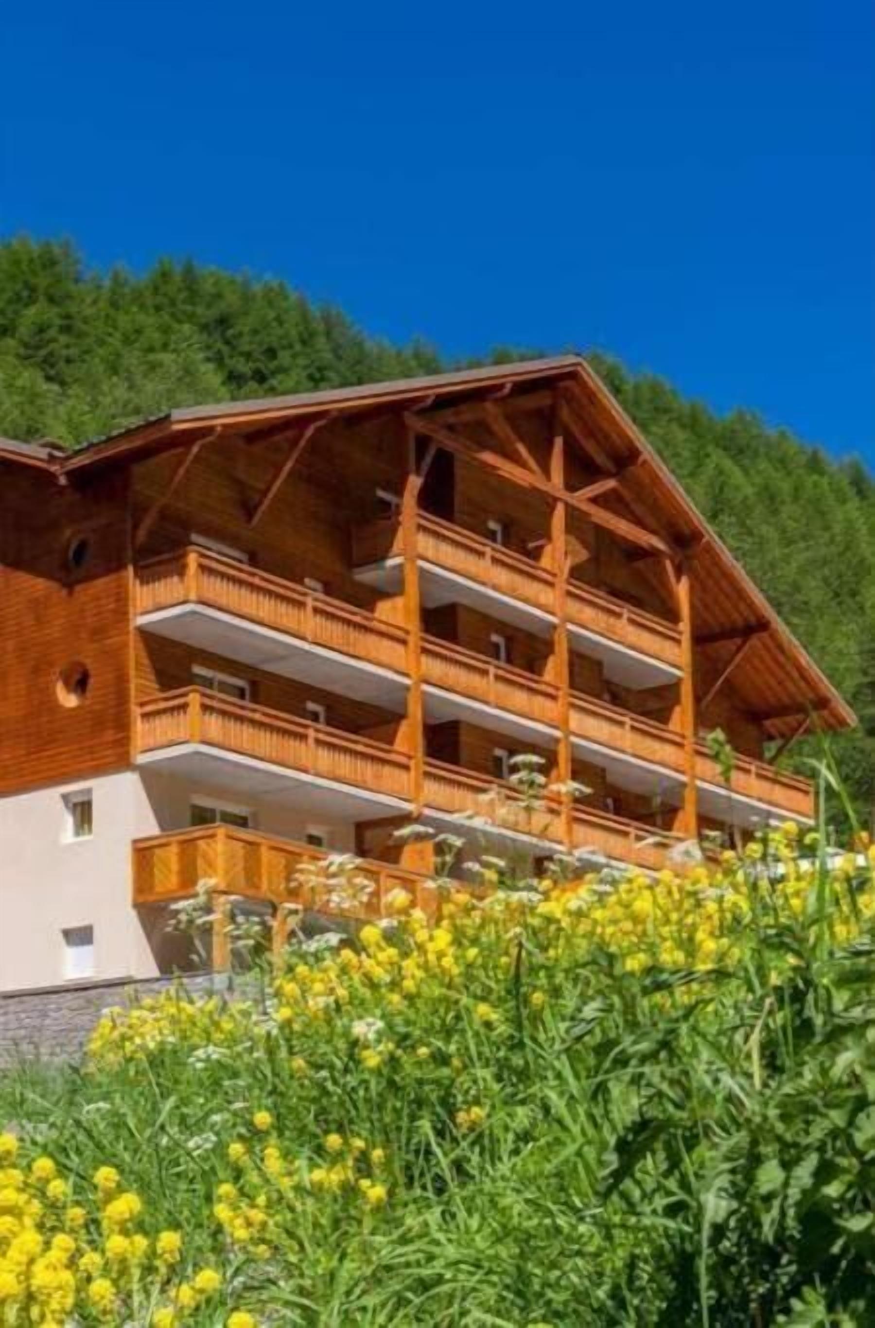 Una cabaña de madera con varios balcones, rodeada de exuberante vegetación y flores amarillas.