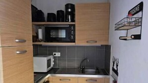 A compact kitchen with wooden cabinets, a microwave, a sink, and a small countertop. - T2 Montagne Cosi Pied des Pistes- Piscine Hammam (Allos)