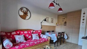 A cozy room with a red patterned sofa, a glass coffee table, and a wooden cabinet. - T2 Montagne Cosi Pied des Pistes- Piscine Hammam (Allos)
