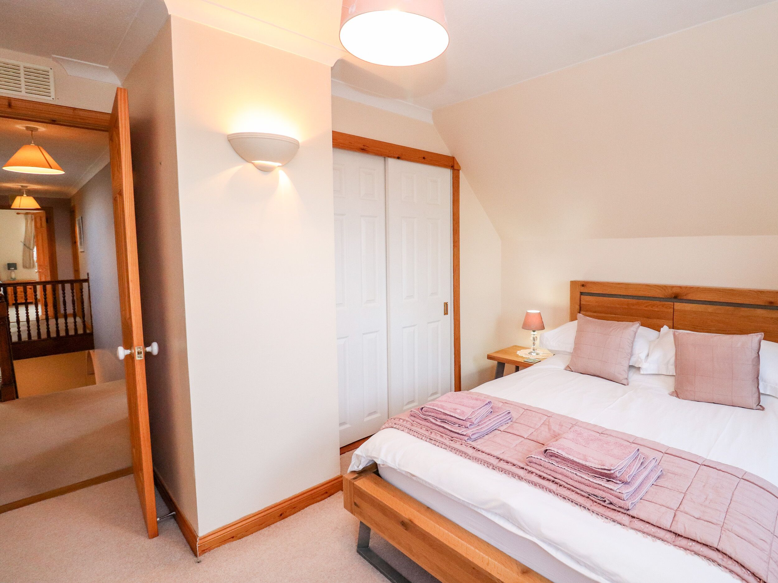 Een slaapkamer met een houten bedframe, een bedlampje en een deur naar een andere kamer.