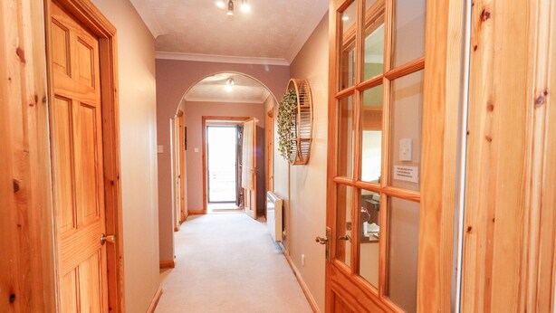 A hallway with wooden doors and a carpeted floor. - Ar Dachaigh (Isle of North Uist)