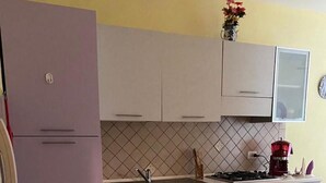 A kitchen with light purple cabinets, a tiled backsplash, a stove, and a coffee maker.