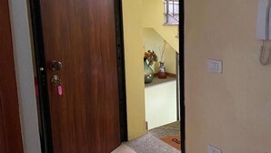 A hallway with a wooden door, a tiled floor, a small table, and a phone on the wall.