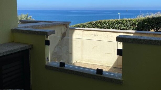A balcony with a view of the ocean, a small window, and wicker furniture.