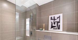 A modern bathroom with a glass shower enclosure, a framed artwork on the wall, and a small shelf with a candle and reed diffuser.