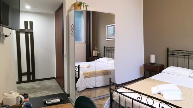 A hotel room with two beds, a desk with a kettle and remote control, a small table, and a painting on the wall. - sansirofiera rooms (Milan)