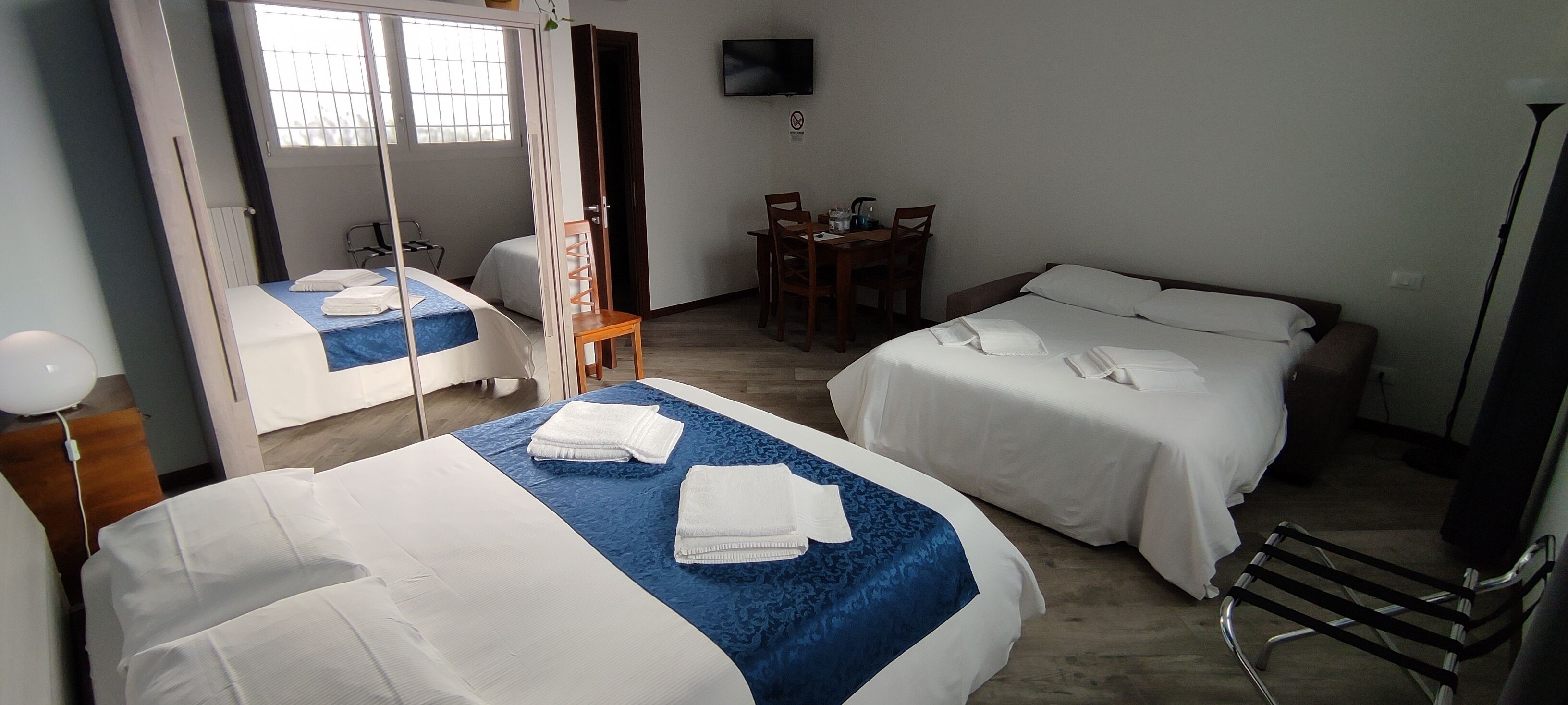 Une chambre d’hôtel avec deux lits, un bureau, une chaise, une télévision et un miroir.
