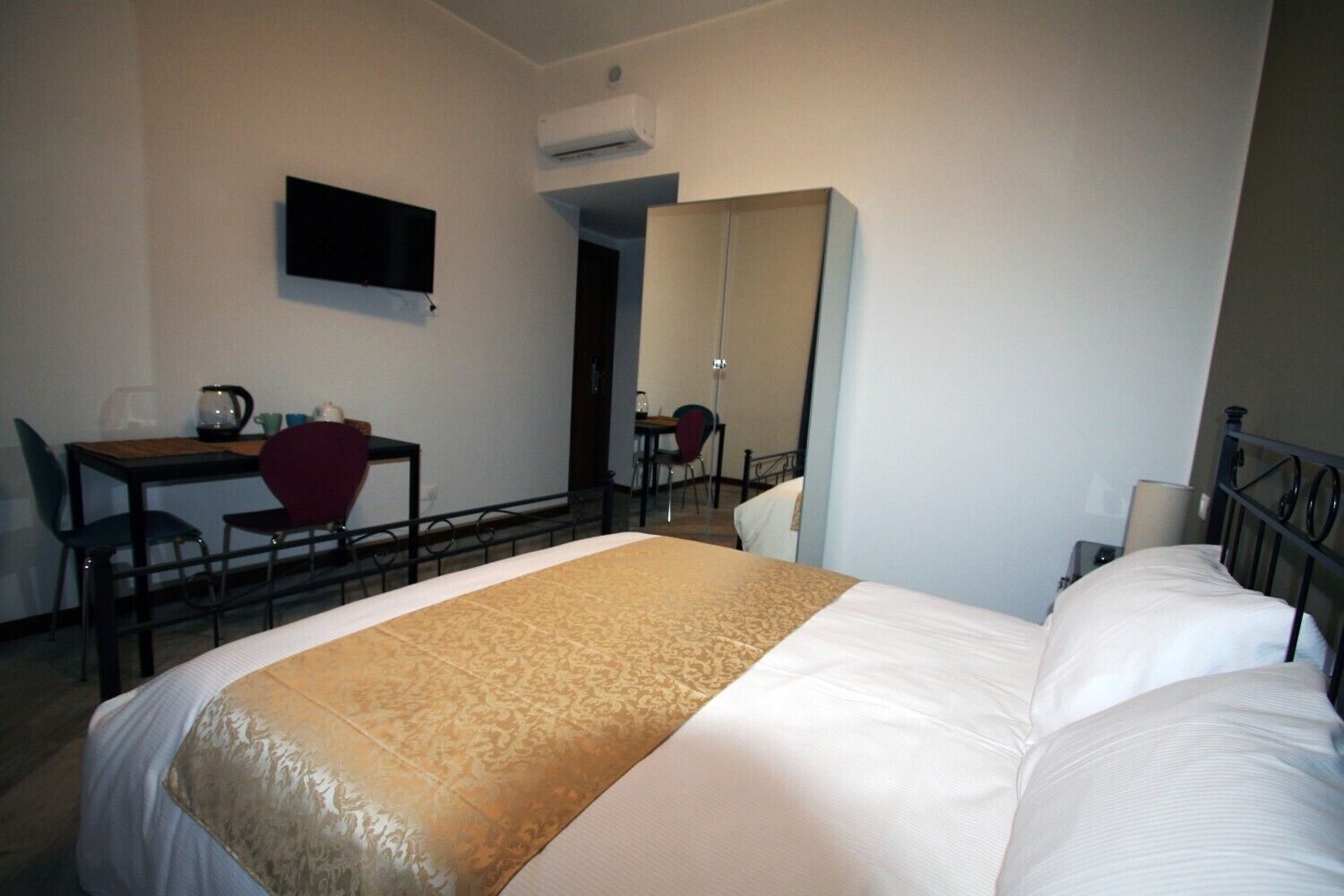 Una habitación de hotel con una cama, un escritorio con sillas, un televisor y un espejo.