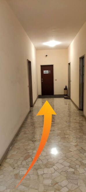 A hallway with a polished stone floor, a brown door at the end, and a directional arrow on the floor. - sansirofiera rooms (Milan)