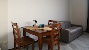 A dining area with a wooden table and chairs, a television mounted on the wall, and a grey sofa. - sansirofiera rooms (Milan)
