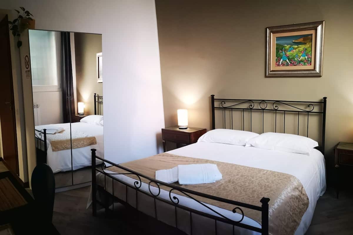 A hotel room with a bed, bedside lamps, a mirror, and a painting on the wall.