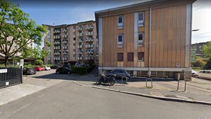 A multi-story residential building with balconies, a parking area, and a motorcycle parked in front. - sansirofiera rooms (Milan)