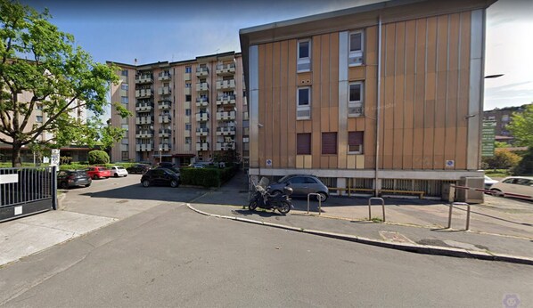 A multi-story residential building with balconies, a parking area, and a motorcycle parked in front. - sansirofiera rooms (Milan)