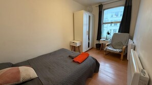 A bedroom with a bed, a chair, a wardrobe, and a window with a view of buildings.