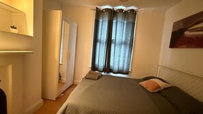 Ein Schlafzimmer mit Bett, Spiegel, einem Fenster mit Vorhängen und einem Bild an der Wand.