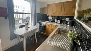 A modern kitchen with wooden cabinets, a gas stove, a microwave, and a sink. - Cosy two bedroom flat Fulham Broadway (London)