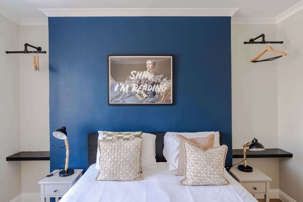 A bedroom with a blue accent wall, a framed picture, two bedside tables, and a bed with patterned pillows.