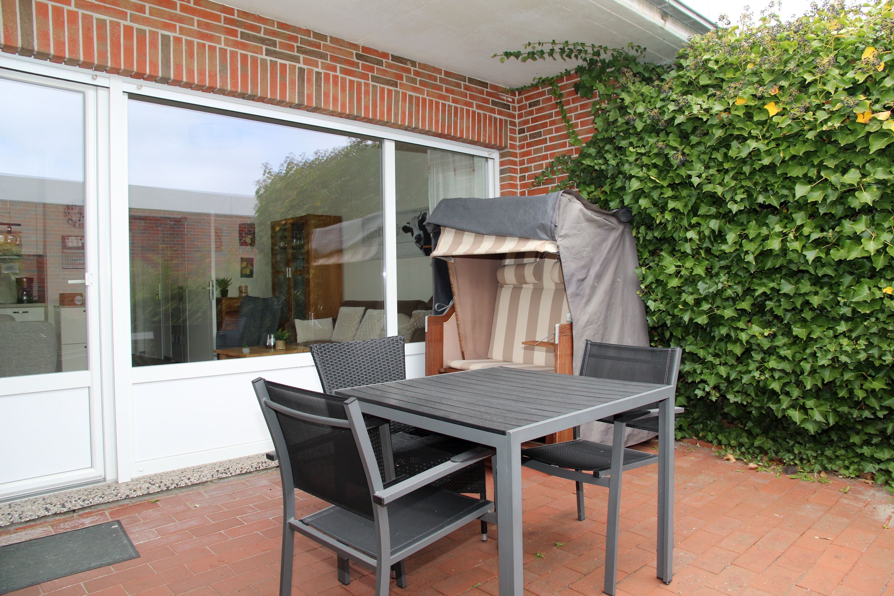 Une terrasse extérieure avec une table et des chaises, un espace salon abrité et un mur de briques agrémenté de verdure.