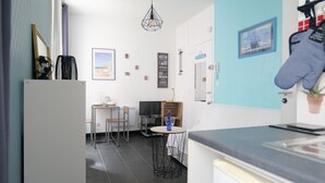 A modern kitchen with a dining area, featuring a kitchen island, dining table, and chairs. There is a hanging light fixture and a wall-mounted oven. - Seafront studio close to all amenities (Les Sables-d´Olonne)