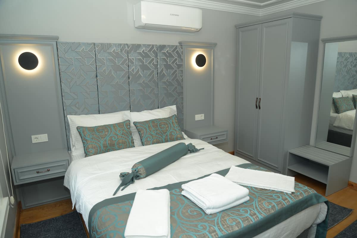 A neatly made bed with a patterned bedspread, a bedside table with a lamp, and a wardrobe with a mirror.