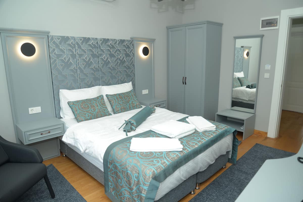 A modern bedroom with a bed, nightstands, a wardrobe, and a mirror.