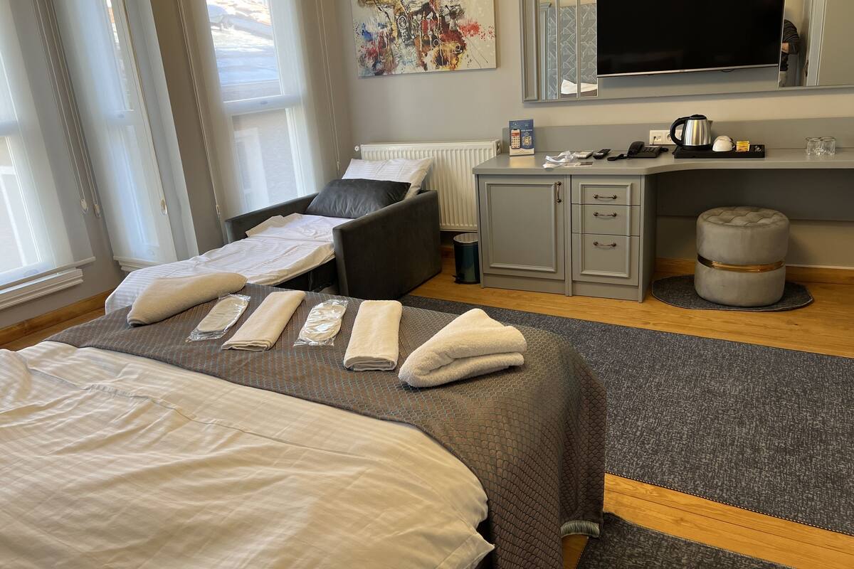 A hotel room with a bed, a desk, a chair, a television, and a window.