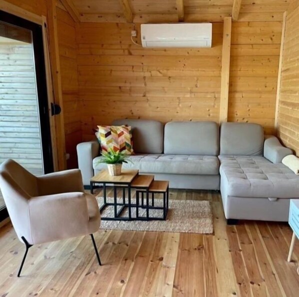 Un interior acogedor de madera, con un sofá gris, una mesita con una planta y una silla.