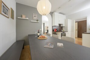 A modern living room with a dark wooden dining table, a large pendant light, and a kitchen area in the background.