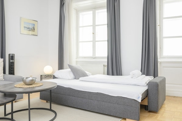 A hotel room with a bed, a round table, a bowl, and a picture on the wall.