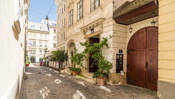 Een smalle straat met kinderaardewerktegels, historische gebouwen, een grote houten deur en potplanten.