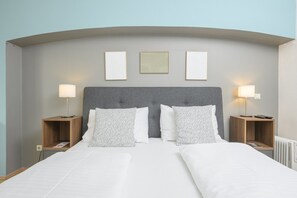 A double bed with a grey upholstered headboard, two bedside tables with lamps, and three framed pictures on the wall.