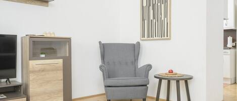 Una sala de estar moderna con un sillón gris, una mesita redonda con una manzana roja y un televisor de pantalla plana sobre un mueble de madera.