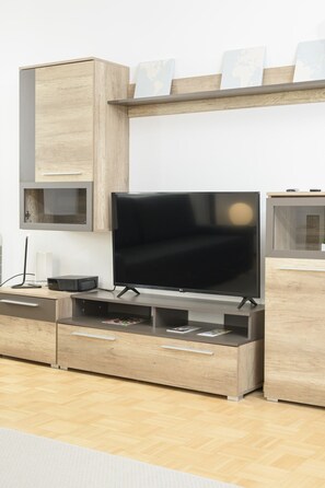 A modern living room with a flat-screen TV, wooden cabinetry, and a built-in shelf with decorative items.
