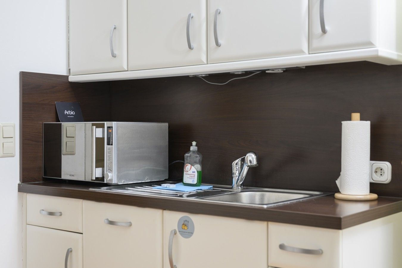 A kitchenette with a microwave, a sink, and a bottle of dish soap.